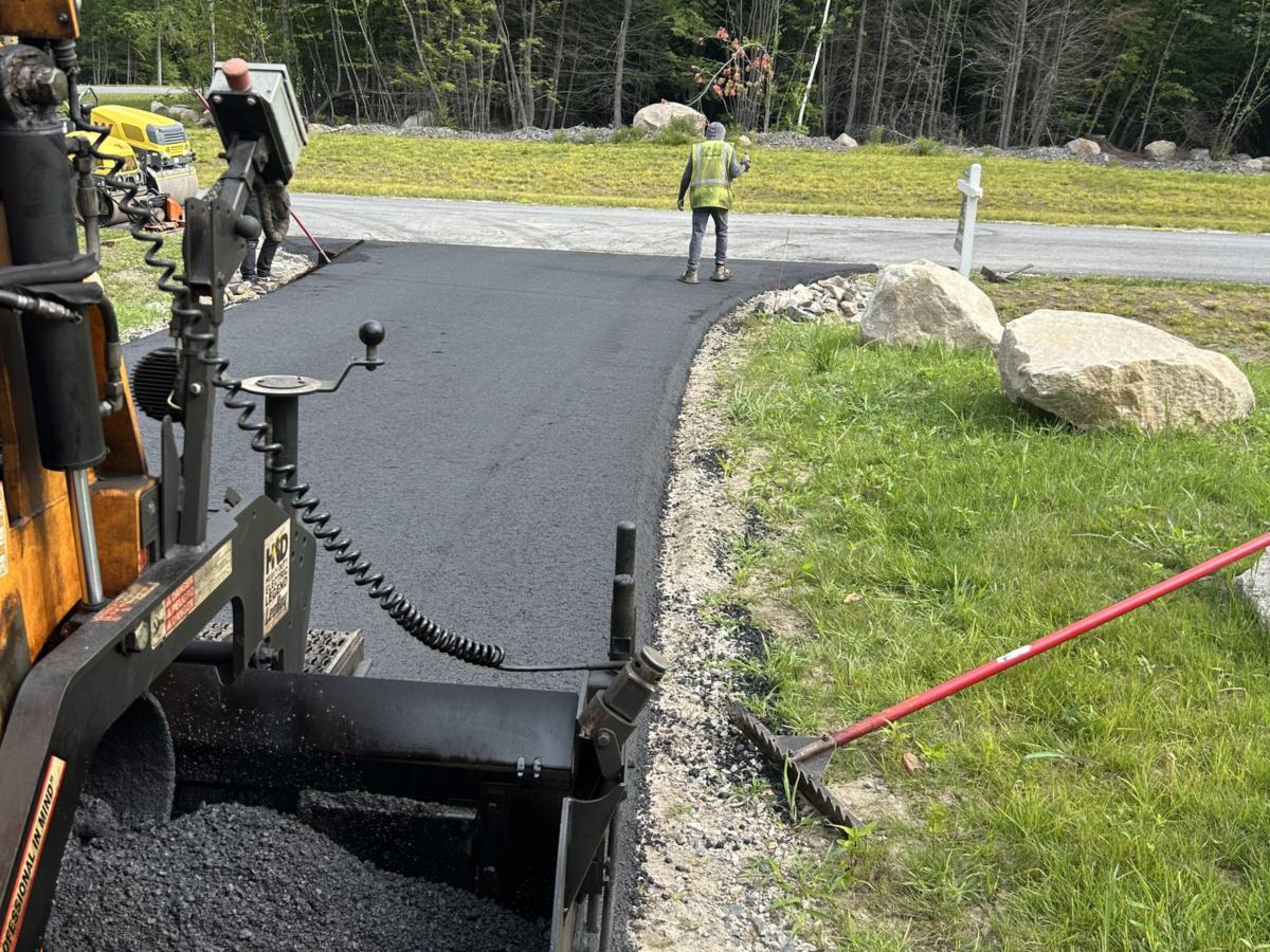 Zilembo's asphalt paver laying a new driveway while a crew member rakes the edge