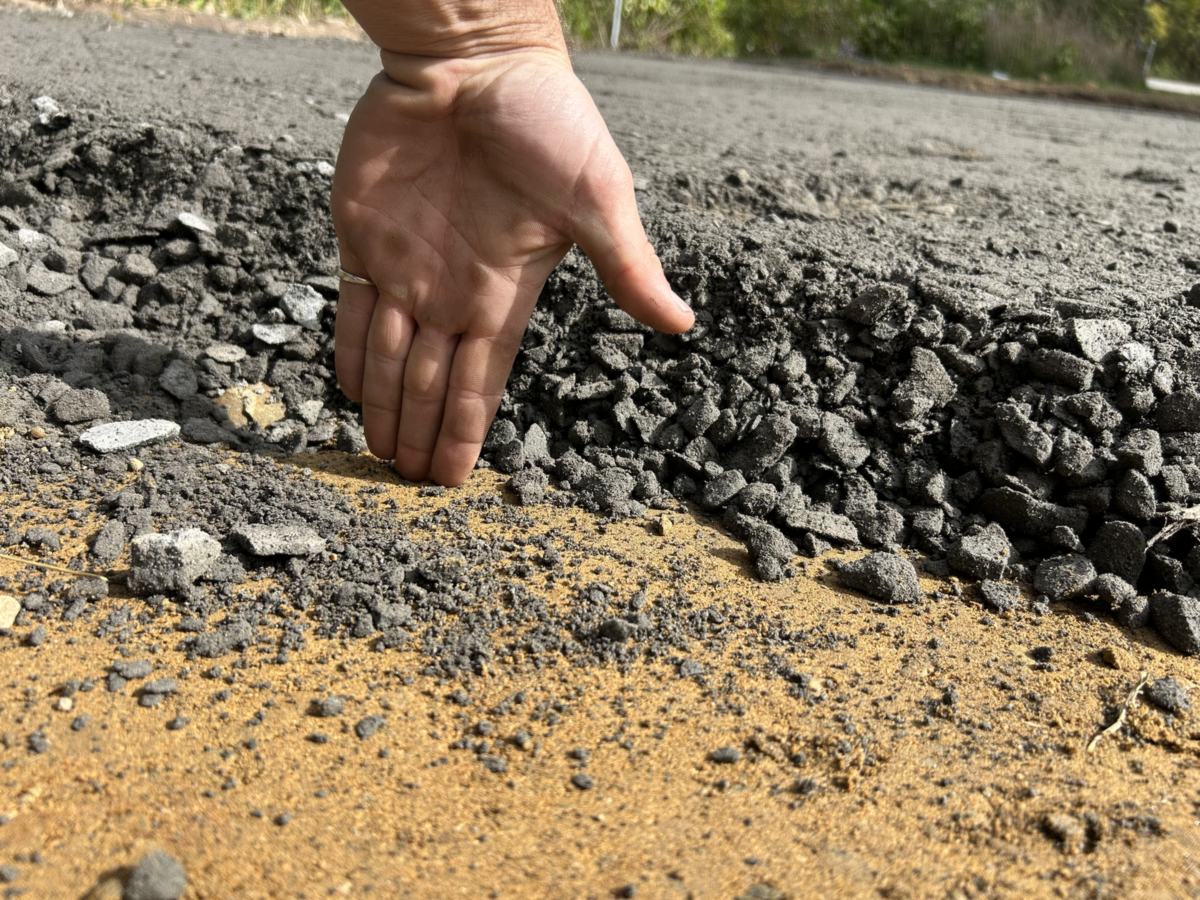 Hand showing the thickness of new asphalt laid over a compacted gravel base