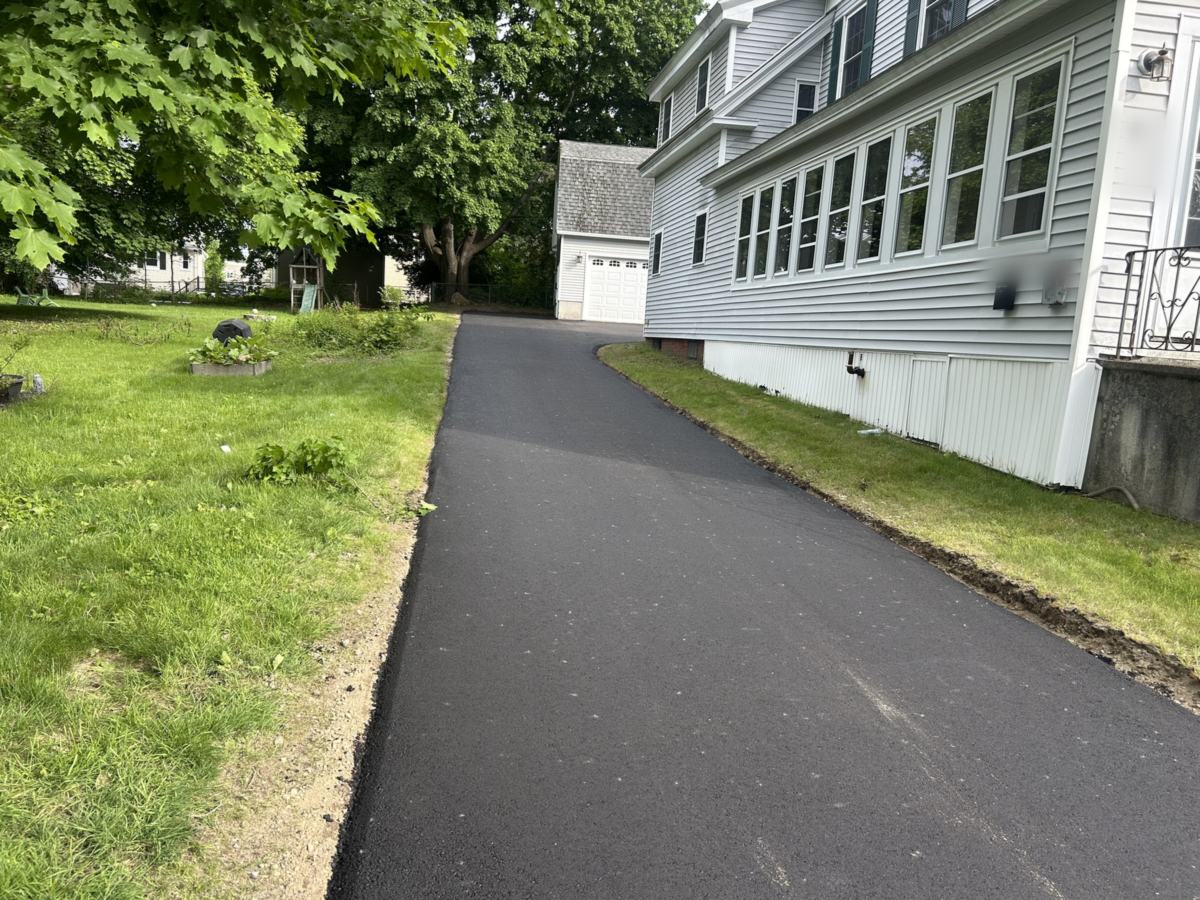 Newly paved asphalt driveway running alongside a house to a detached garage in Berwick, Maine