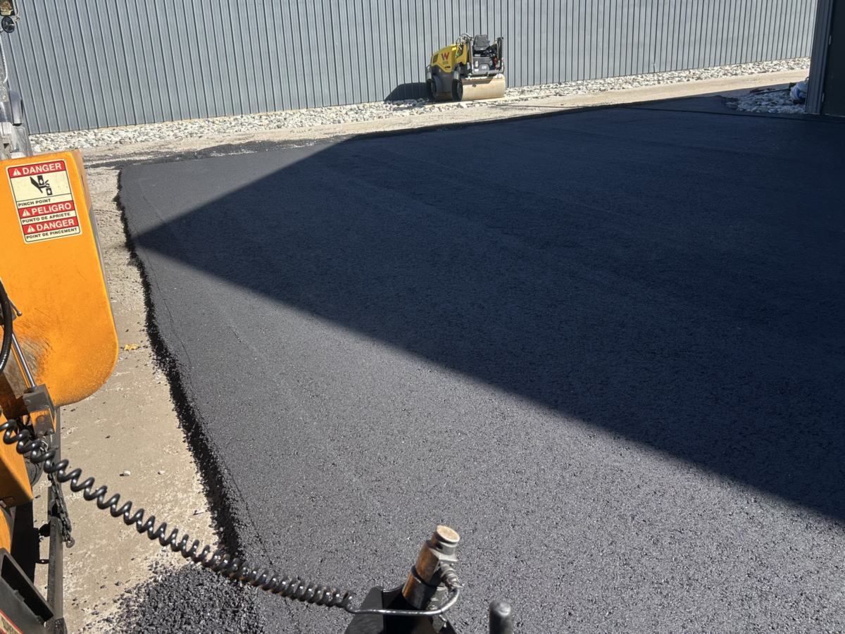 Asphalt paver laying a new commercial lot beside a metal building in Southern Maine