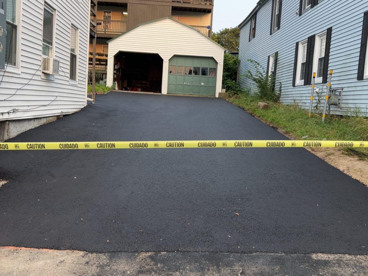 Newly paved asphalt driveway between two houses leading to a detached garage