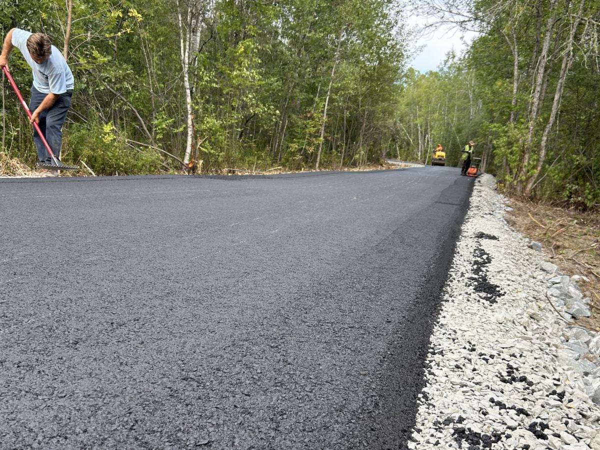 Zilembo's crew raking the edge of a freshly paved road through the woods in Southern Maine
