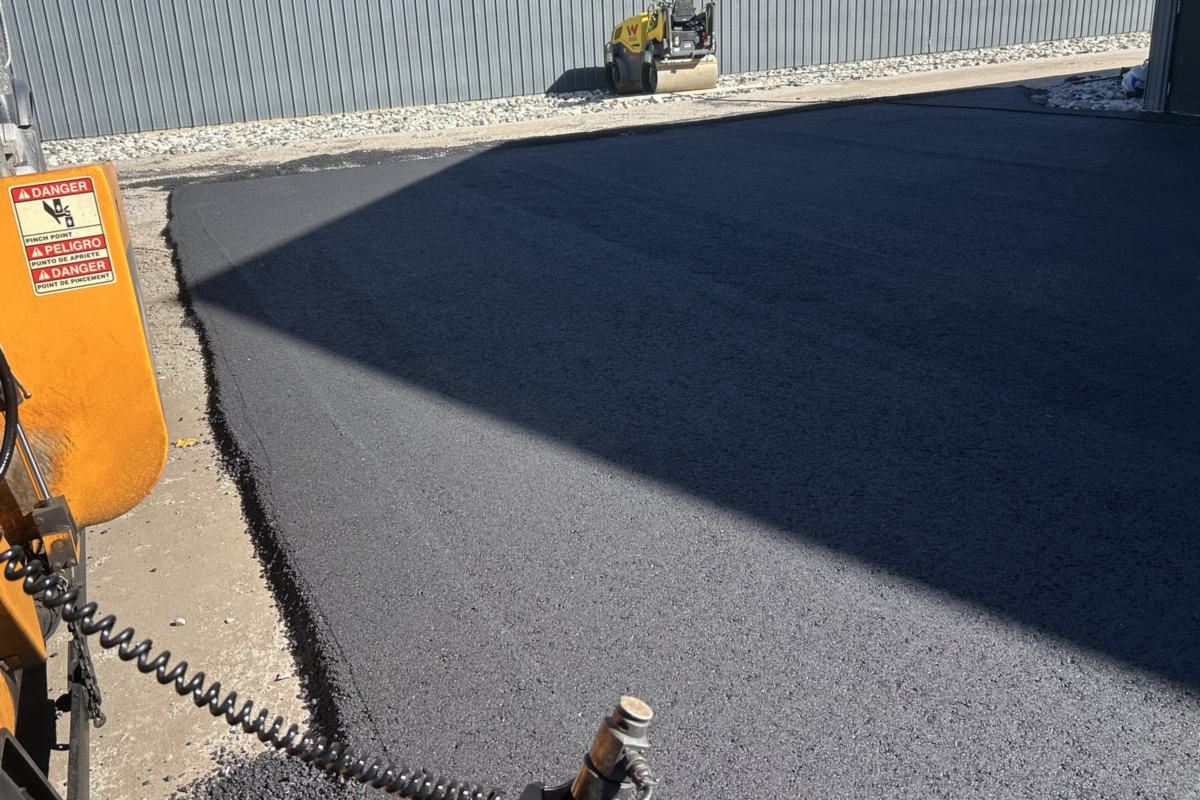 Asphalt paver laying a new commercial lot beside a metal building in Southern Maine