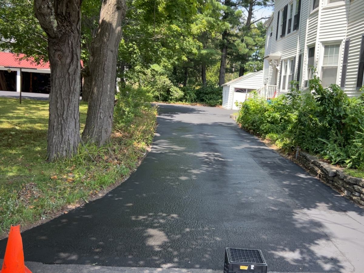 Curved residential driveway after sealcoating, edged by a stone wall in Southern Maine