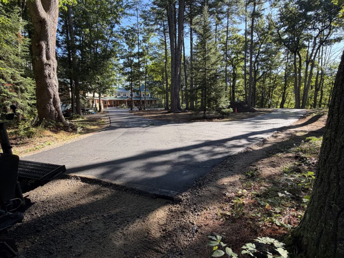 New asphalt driveway winding through tall pine trees to a home in Southern Maine